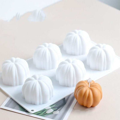 White silicone candle mold with six pumpkin-shaped cavities and one finished orange pumpkin candle on a table
