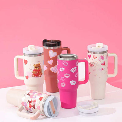 Geïsoleerde Tumbler met handvat en rietje in verschillende kleurrijke, feestelijke designs met hart- en lippenstiftprints, perfect voor warme en koude dranken.